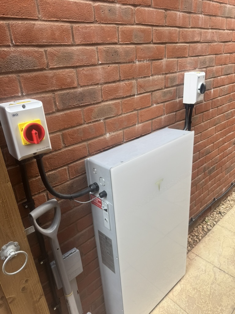 Tesla home battery installed against a brick wall with electrical isolators